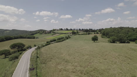 Drone-shot-of-winding-roads-and-golden-farm-fields-in-Tuscany-Italy-landscape-on-a-sunny-day-with-blue-sky-and-clouds-on-the-horizon-LOG
