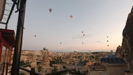 View-of-the-hot-air-balloons-floating-in-the-air-from-one-of-the-famous-cave-hotels-located-in-the-historical-ancient-rock-structures-in-Cappadocia,-Turkey