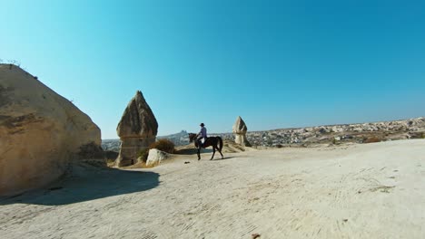Male-Tourist-Riding-A-Horse-In-Cappadocia,-Turkey-On-A-Sunny-Day---Drone-FPV