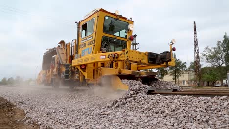 Yellow-railroad-track-laying-machine-in-operation-on-a-cloudy-day,-spreading-gravel-on-tracks