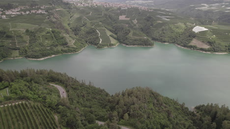 Drone-shot-flying-over-Lago-di-Santa-Giustina-near-Trentino-in-Italy-on-a-cloudy-day-with-mountains-and-water-surrounded-by-green-fields-and-trees-LOG