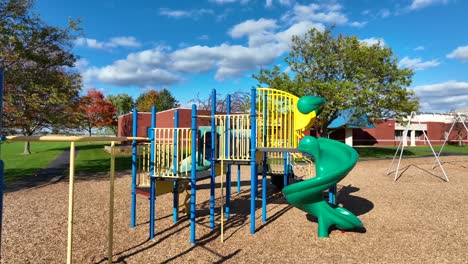 Colorful-playground-with-slides-and-swings,-sunny-day,-school-in-background