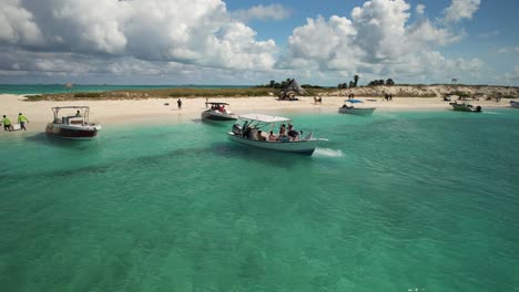 Boote-Auf-Klarem-Türkisfarbenem-Wasser-In-Der-Nähe-Des-Sandstrandes-Von-Los-Roques,-Venezuela,-Mit-Menschen-Und-Strandhütten,-Luftaufnahme