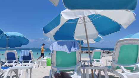 Embrace-the-Caribbean-allure:-Empty-chairs-with-umbrellas-adorn-the-sandy-shore,-framed-by-vivid-blue-waters-and-skies,-evoking-serenity-and-tropical-bliss