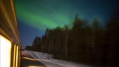 Outside-view-of-train-traveling-through-a-snowy-forest-with-green-northern-lights-lighting-up-the-sky