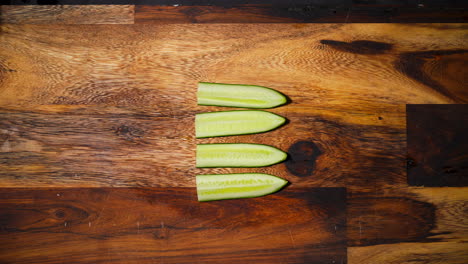 Top-view-of-a-male-hand-slicing-two-pieces-of-cucumber-perpendicular-in-the-middle