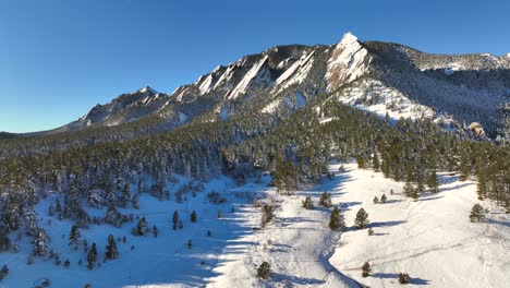 Slow-aerial-drone-rise-with-view-of-Boulder-flatirons-at-sunrise-on-a-bright-winter-day-with-nature-landscape-and-park-in-view