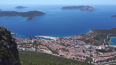 Drone-panning-from-the-left-to-the-right-side-of-the-frame-overlooking-the-beachfront-of-the-town-of-Kaş,-including-the-nearby-islands-in-the-Mediterranean-Sea,-in-Antalya-province-in-Turkey