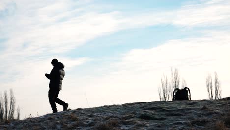 Person-in-black-jacket-walk-on-rocky-hill-and-leave-backpack,-drone-follow