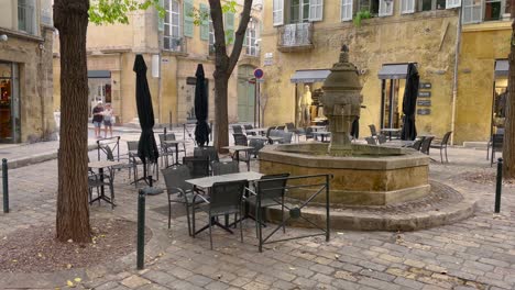 Tables-by-fountain-in-Aix-en-Provence-old-town,-tourist-couple-with-map-in-background