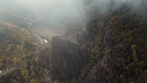 drone-shot-revealing-gouffre-d'enfer-dam-near-saint-etienne-on-a-moody-day-with-fog-and-low-clouds,-fance