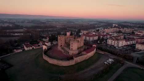 drone-shot-approaching-Montrond-les-bains-Castle-during-the-sunrise-with-a-beautiful-golden-hour,-Plaine-du-Forez,-Loire-departement,-French-Countryside