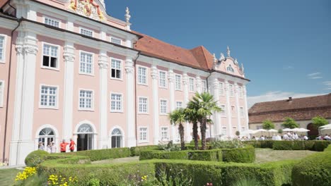 Sonniger-Tag-Am-Rosafarbenen-Schloss-Meersburg-Am-Bodensee-Mit-Touristen-Und-Palmen-Im-Vordergrund