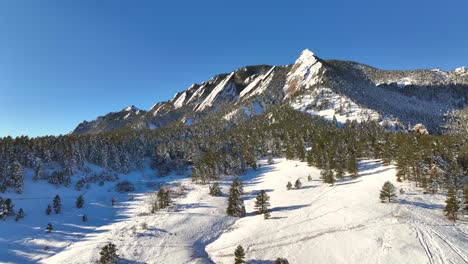 Aerial-flyover-of-chautauqua-park-flatirons-nature-landscape-in-Boulder,-Colorado,-USA-on-a-bright-winter-day-with-snow-covering-ground