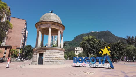 Simon-Bolivar-Statue-At-Journalists-Park-Gabriel-García-Márquez-Next-To-Blue-Bogota-Sign-On-Sunny-Day