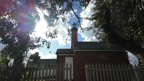 Amidst-the-tranquil-outdoor-setting,-a-stately-brick-building-with-a-lighthouse-stands-tall,-framed-by-a-white-fence-and-adorned-with-windows-that-offer-glimpses-of-the-vast-sky-and-passing-clouds