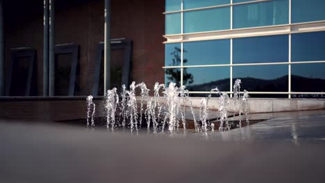 Static-shot-of-water-splashing-from-water-fountain-in-front-of-Glass-modern-building