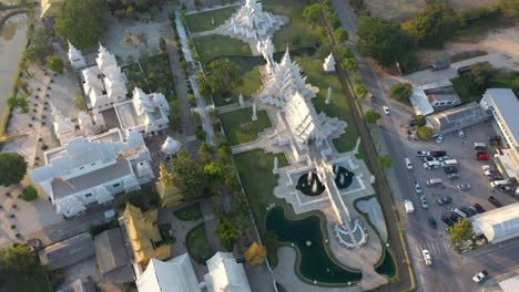 Aerial-drone-birds-eye-view-of-Wat-Rong-Khun-the-giant-buddhist-White-Temple-and-Golden-Temple-with-mountains-and-landscape-in-Chiang-Rai,-Thailand