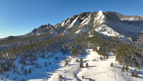 Slow-drone-aerial-fly-in-towards-the-dramatic-Flatiron-mountains-in-Boulder,-Colorado-on-a-sunny-winter-day