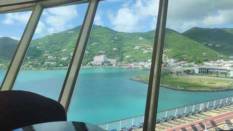 Marvel-at-the-Caribbean's-allure:-Through-vast-window,-behold-panoramic-vista-of-lush-island-landscapes-and-towering-mountains,-embraced-by-the-tranquil-sea