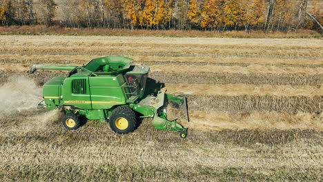 Tracking-drone-shot-of-a-John-Deere-combine-picking-up-a-canola-swath