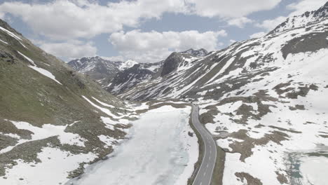 Drone-shot-flying-over-a-single-road-in-between-snow-mountains-at-the-Fluela-Pass-in-Switzerland-on-a-cloudy-and-cold-day-with-clear-sight-LOG