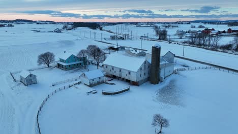 Rural-farm-covered-in-snow-during-winter-sunset-in-American-countryside