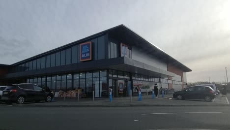 Time-lapse-shoppers-enter-busy-Aldi-supermarket-entrance-with-people-and-cars-passing-outside