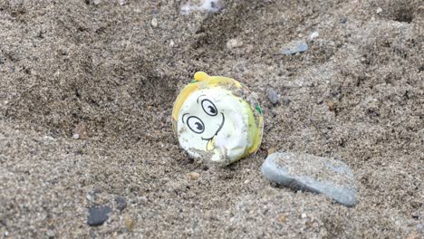 Close-up-of-ocean-plastic-with-happy-smiley-face-laying-on-a-sandy-beach-polluting-the-sea-and-coastline-on-a-remote-tropical-island-destination
