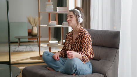Young-relaxed-happy-woman-listens-to-music-in-headphones-at-home,-pan