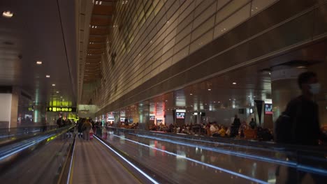 Person-Mit-Einem-Koffer,-Die-über-Eine-Rolltreppe-Läuft-Und-Dabei-Eine-Mundmaske-Am-Flughafen-Doha-Trägt