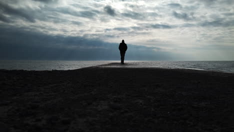 Man-in-a-black-coat-walking-on-a-concrete-jetty-to-the-infinite-horizon-of-Lake-Ontario