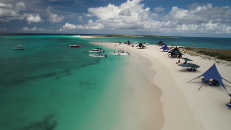 1Los-roques-archipelago-with-clear-turquoise-waters,-white-sandy-beach,-boats,-and-visitors-under-tents,-aerial-view