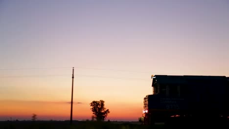 Train-silhouette-against-a-vibrant-sunset-in-the-countryside,-early-evening