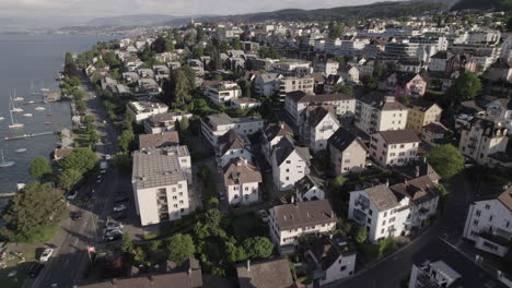 Drone-shot-flying-near-the-city-of-Thalwil-at-the-Zurich-Lake-in-Switzerland-on-a-sunny-day-with-water-and-boats-around-the-shore-and-white-houses-in-the-city-LOG