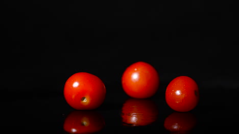 Seitenansicht-Von-Drei-Tomaten,-Die-In-Zeitlupe-Auf-Eine-Schwarze-Reflektierende-Oberfläche-Fallen