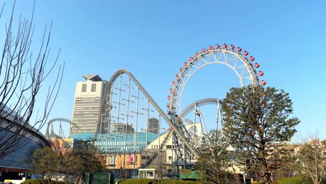 Skyline-view-of-a-Ferris-wheel-and-roller-coaster-in-an-amusement-park-with-city-buildings-in-the-background,-clear-day