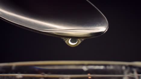Droplets-drip-slowly-off-of-metal-spoon-into-glass,-macro-closeup-in-slow-motion