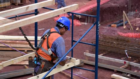 Construction-worker-in-orange-vest-and-blue-helmet-working-on-scaffolding-at-a-building-site,-daytime