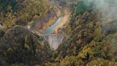 aerial-shot-of-a-dam-through-clouds-and-fog,-gouffre-d'enfer-dam-in-France-near-Saint-Etienne-during-fall,-loire-departement,-France