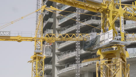 An-observation-of-a-skyscraper-under-construction,-ascending-to-a-minimum-of-100-meters,-accompanied-by-yellow-cranes-diligently-laboring-on-this-impressive-edifice