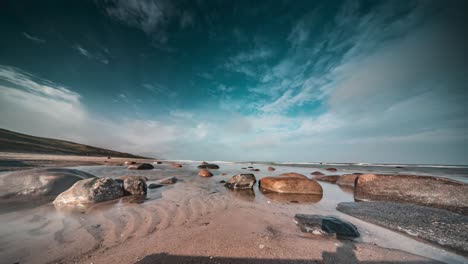 Light-white-clouds-fly-above-the-rocky-beach-as-the-waves-slowly-roll-over-the-stones