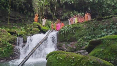 Group-of-natives-in-traditional-attire-celebrating-on-a-lush-green-forest-backdrop-with-a-waterfall-in-Oxapampa,-Peru