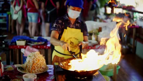 Chef-Tailandés-Usando-Un-Wok-En-Llamas-Para-Cocinar-Fideos-Salteados