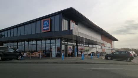 Time-lapse-shoppers-enter-and-leave-Aldi-supermarket-with-cars-passing-and-parking