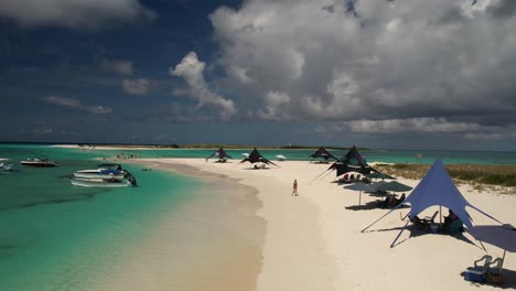 Los-roques-archipelago-with-clear-turquoise-waters,-white-sands,-and-visitors-under-sunshades,-boats-anchored-nearby,-aerial-view