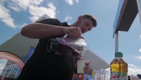 Low-angle-view-of-a-young-man-pouring-smoothie-at-a-glass-under-clear-sky-at-Tour-De-France-in-France