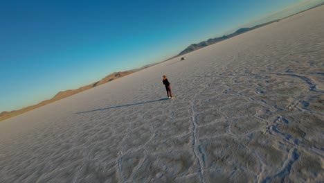 FPV-Drone-Flying-Around-Operator-And-Car-Driving-On-Bonneville-Salt-Flats-In-Utah-During-Golden-Hour