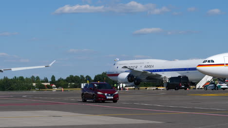 Coche-Rojo-Conduciendo-En-La-Pista-Del-Aeropuerto-De-Vilnius-Pasando-El-Código-Uno-De-Corea-Aviones-Que-Asisten-A-La-Cumbre-De-La-OTAN-En-Lituania