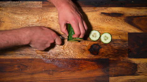Top-view-of-a-male-hand-chopping-a-fresh-cucumber-on-cutting-board-in-slowmotion